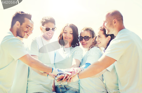 Image of group of volunteers putting hands on top in park