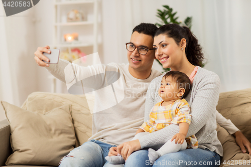 Image of mother and father with baby taking selfie at home