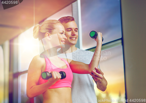 Image of smiling young woman with personal trainer in gym