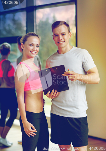 Image of smiling young woman with personal trainer in gym