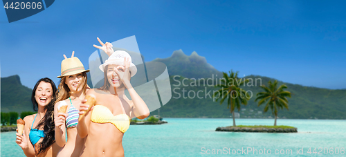 Image of group of smiling women eating ice cream on beach