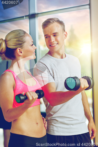 Image of smiling young woman with personal trainer in gym