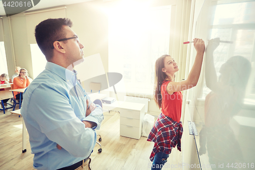 Image of teacher and student writing on board at school