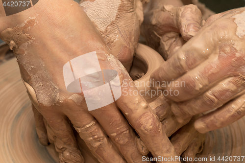 Image of Beginner and teacher in process of making clay bowl on pottery w