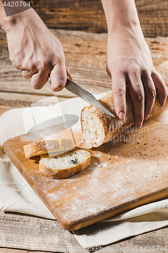 Image of Whole grain bread put on kitchen wood plate with a chef holding gold knife for cut.