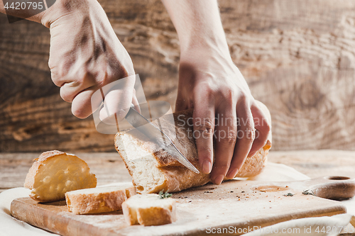 Image of Whole grain bread put on kitchen wood plate with a chef holding gold knife for cut.