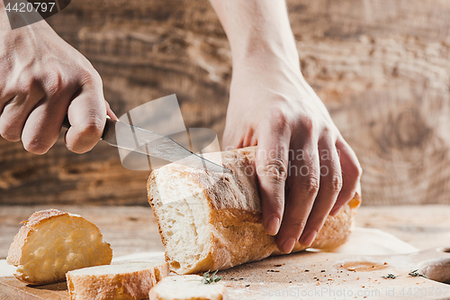 Image of Whole grain bread put on kitchen wood plate with a chef holding gold knife for cut.