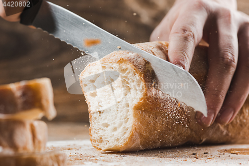 Image of Whole grain bread put on kitchen wood plate with a chef holding gold knife for cut.