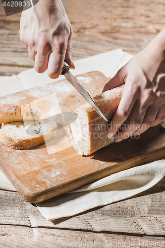 Image of Whole grain bread put on kitchen wood plate with a chef holding gold knife for cut.