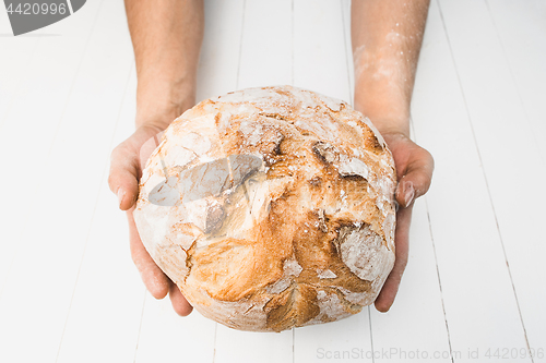 Image of Closeup of male hands put fresh bread on an old rustic table on black background with copy space for your text