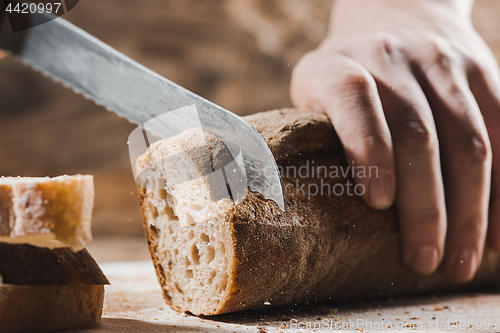 Image of Whole grain bread put on kitchen wood plate with a chef holding gold knife for cut.