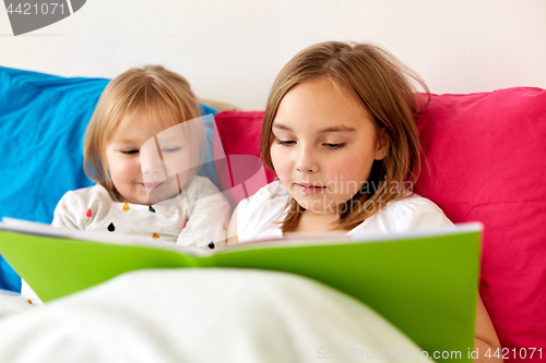 Image of little girls or sisters reading book in bed