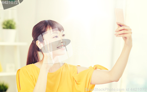 Image of happy asian woman taking selfie with smartphone