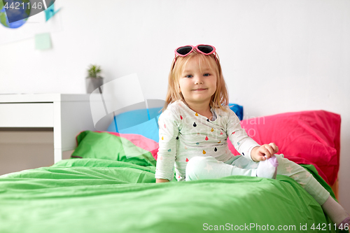 Image of smiling little girl with sunglasses on bed at home