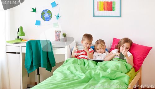 Image of kids with tablet pc and smartphones in bed at home