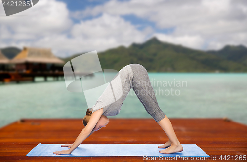 Image of woman making yoga dog pose on mat outdoors