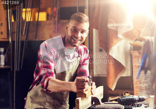 Image of carpenter working with plane and wood at workshop