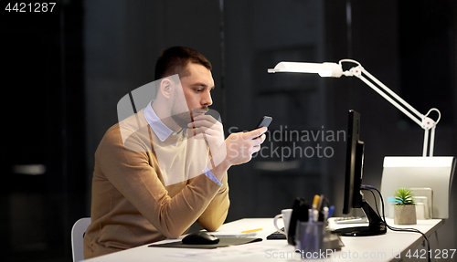 Image of man with smartphone working late at night office