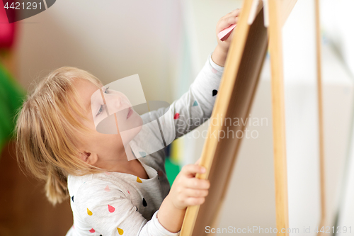 Image of happy little girl drawing on chalk board at home