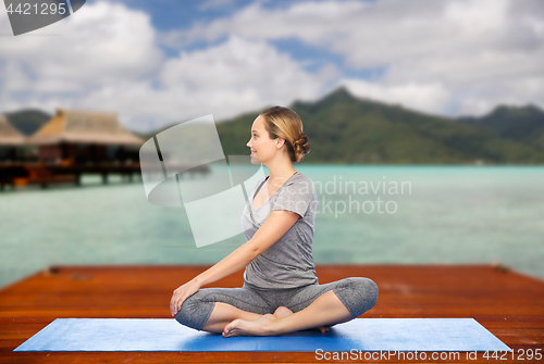 Image of woman making yoga in twist pose on mat outdoors