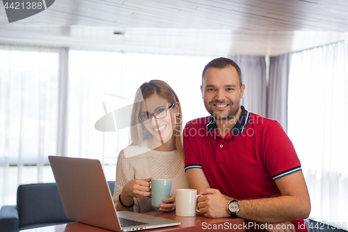 Image of couple drinking coffee and using laptop at home