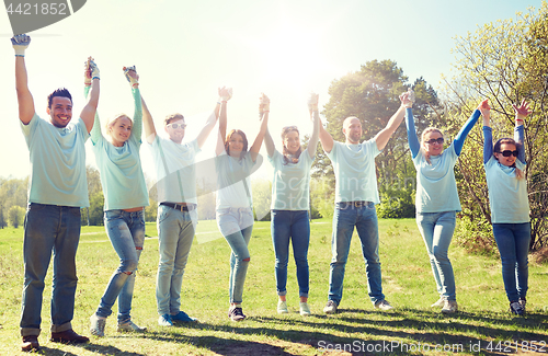 Image of group of happy volunteers holding hands outdoors