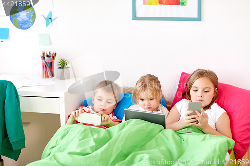 Image of kids with tablet pc and smartphones in bed at home