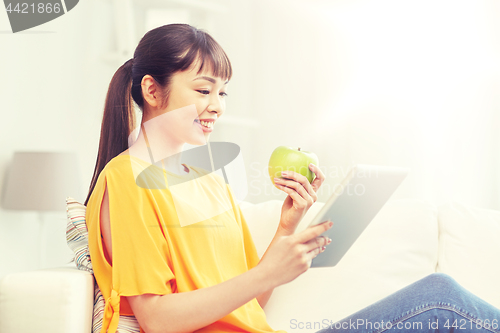 Image of happy asian woman with tablet pc and apple at home