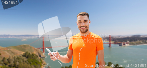 Image of man with smartphone and earphones over golden gate