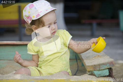 Image of Little girl is playing in the old sandbox