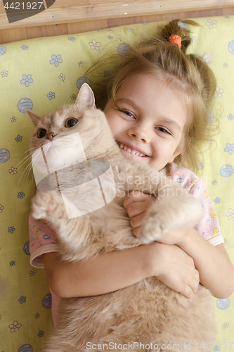 Image of Little girl hugging a cat lying on a mattress on the floor