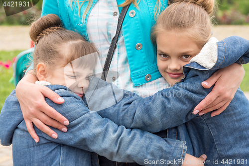 Image of Two girls hug mother tightly