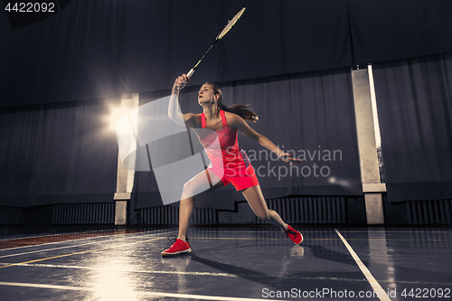 Image of Young woman playing badminton at gym