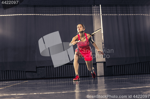 Image of Young woman playing badminton at gym