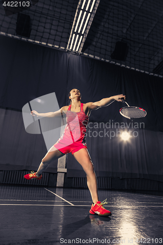 Image of Young woman playing badminton at gym