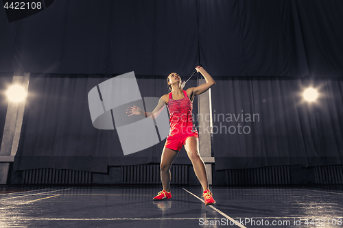 Image of Young woman playing badminton at gym