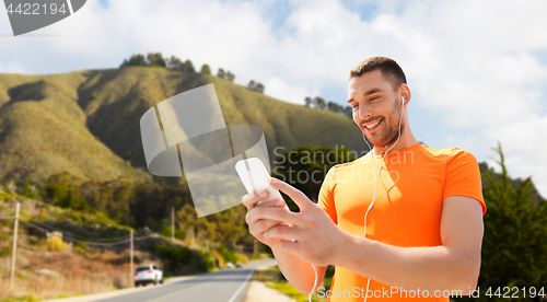 Image of man with smartphone and earphones over hills