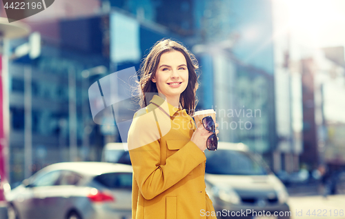 Image of happy young woman drinking coffee on city street