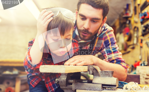Image of father and little son with wood plank at workshop