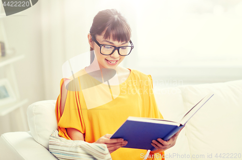 Image of smiling young asian woman reading book at home