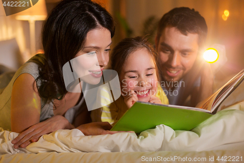 Image of happy family reading book in bed at night at home