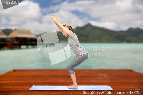 Image of woman making yoga in chair pose on mat outdoors