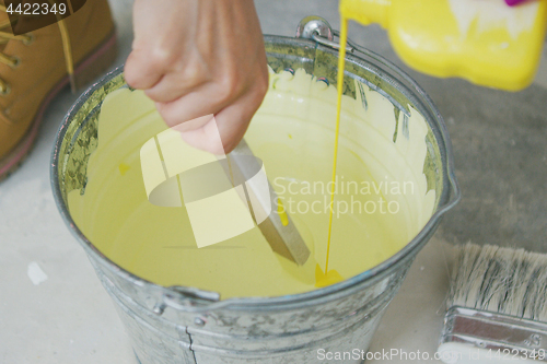 Image of Hand mixing yellow wall paint in bucket 