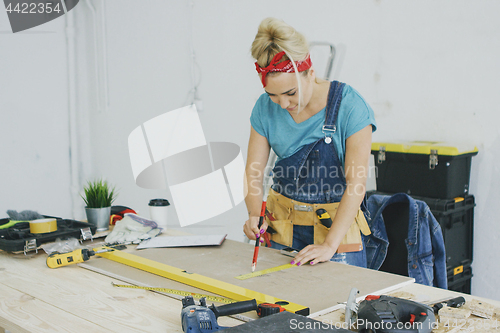 Image of Woman drawing line on plywood in workshop 