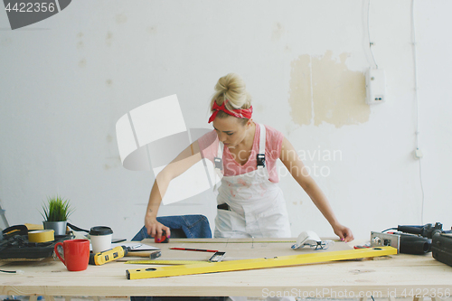 Image of Female carpenter measuring wood on workbench 