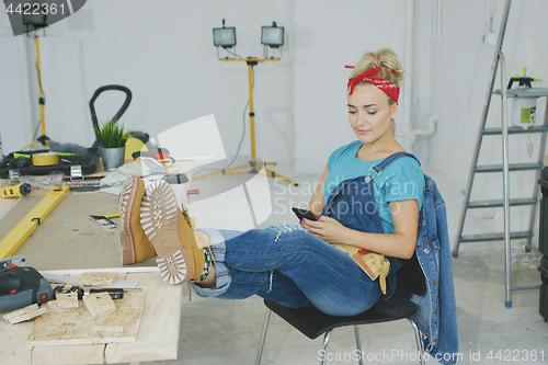 Image of Woman resting with smartphone at carpenter workbench 