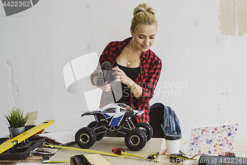 Image of Woman playing with radio-controlled car in workshop
