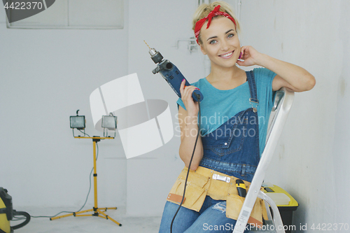 Image of Happy woman with drill sitting on stepladder 