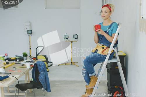 Image of Female carpenter resting on stepladder with beverage 