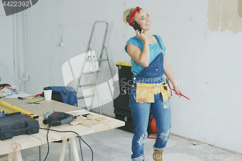 Image of Cheerful female carpenter talking on smartphone 